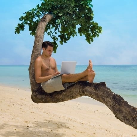 Homme avec un ordinateur sur une grosse branche d'arbre devant la plage