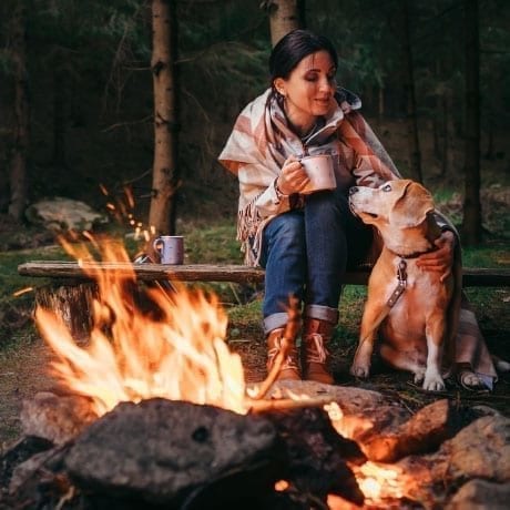 Femme avec son chien devant un feu de camp